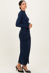 woman wearing a navy blue glitter long sleeve dress with ruching details and a side slit, standing sideways