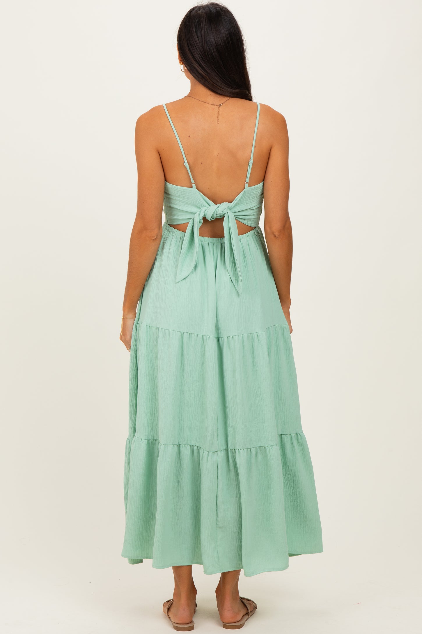 woman wearing a mint green tiered maxi dress with thin straps and a tied back detail