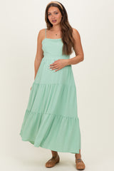 woman wearing a mint green maternity maxi dress with tiered ruffles and holding her baby bump