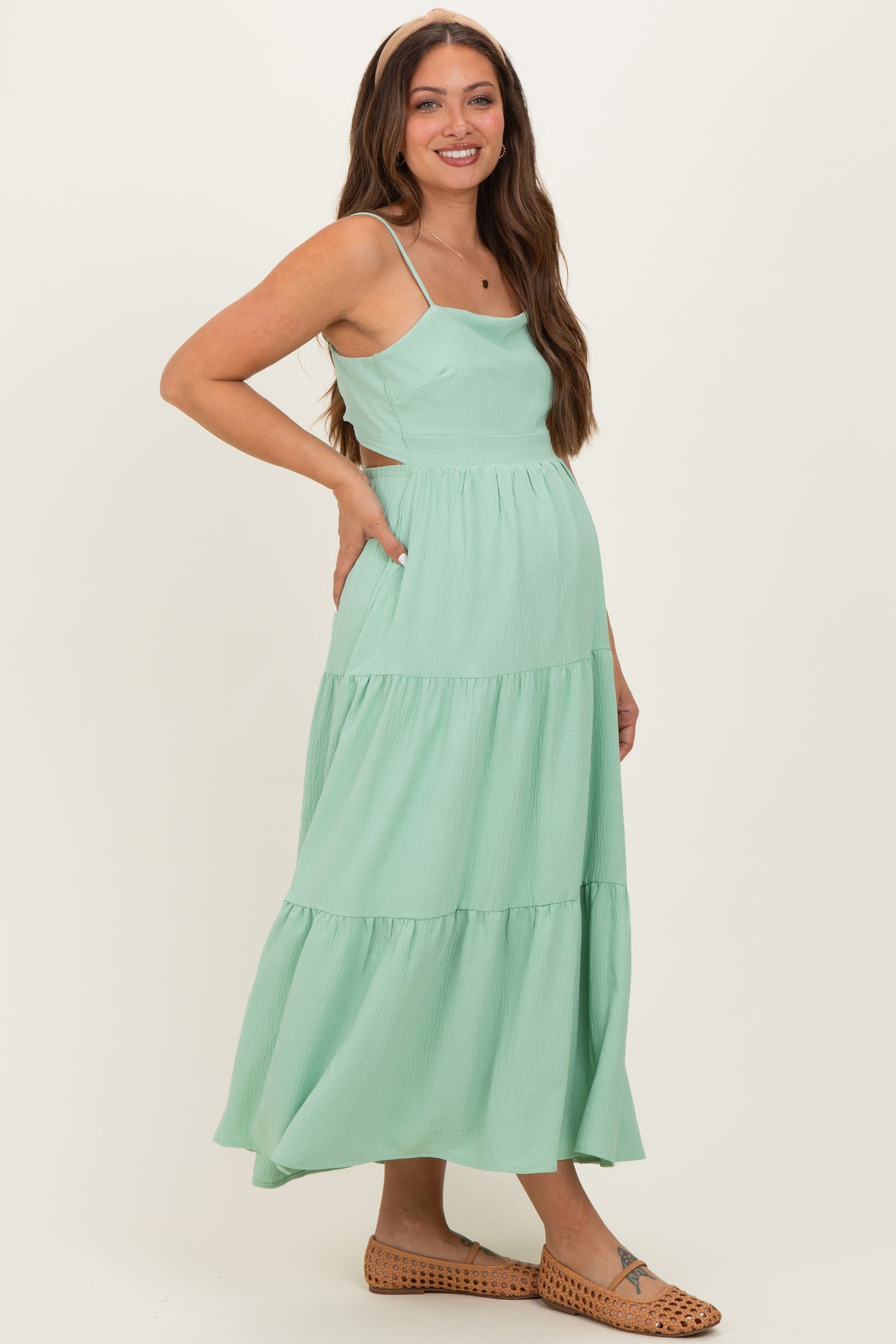 woman wearing a mint green maternity maxi dress with tiered ruffles and a fitted bodice, showing her baby bump