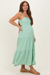 woman wearing a mint green maternity maxi dress with tiered ruffles and a fitted bodice, showing her baby bump