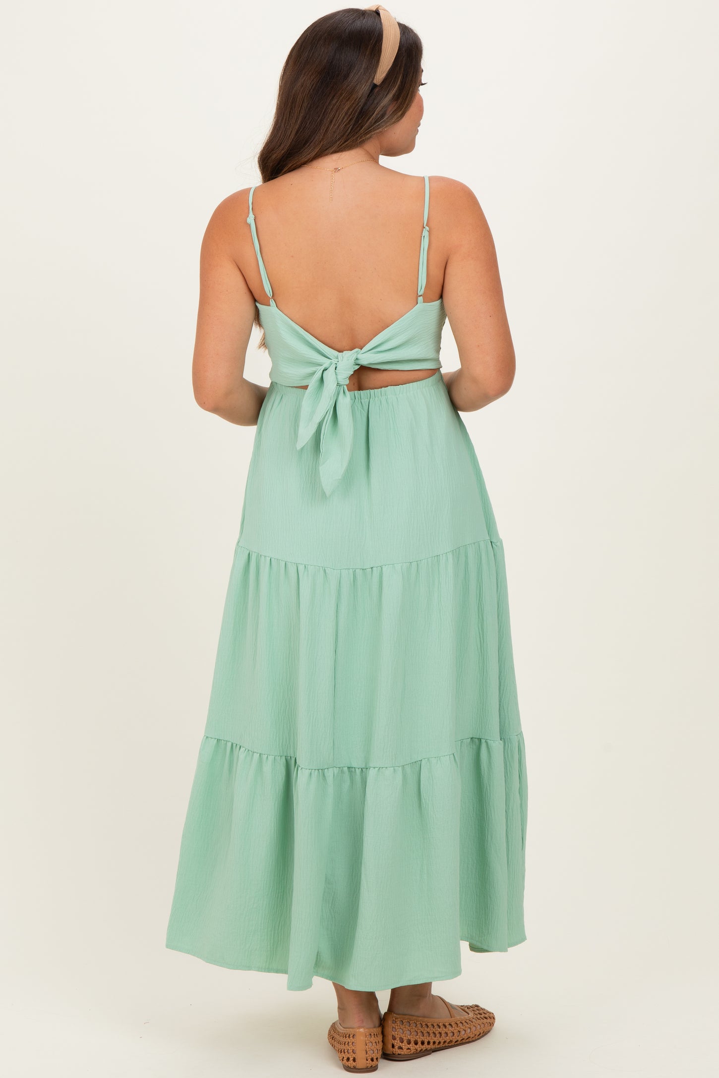 woman wearing a mint green maternity maxi dress with a tied back and tiered skirt