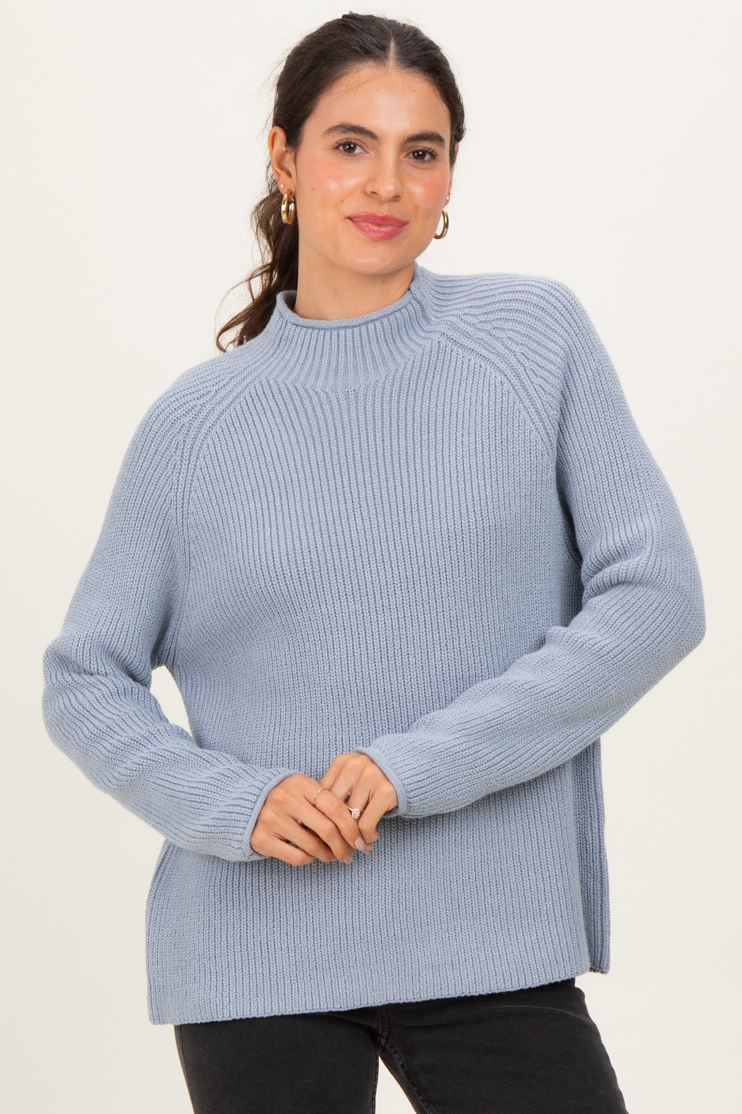 woman wearing a light blue ribbed sweater with a high neckline and long sleeves, posing with a smile