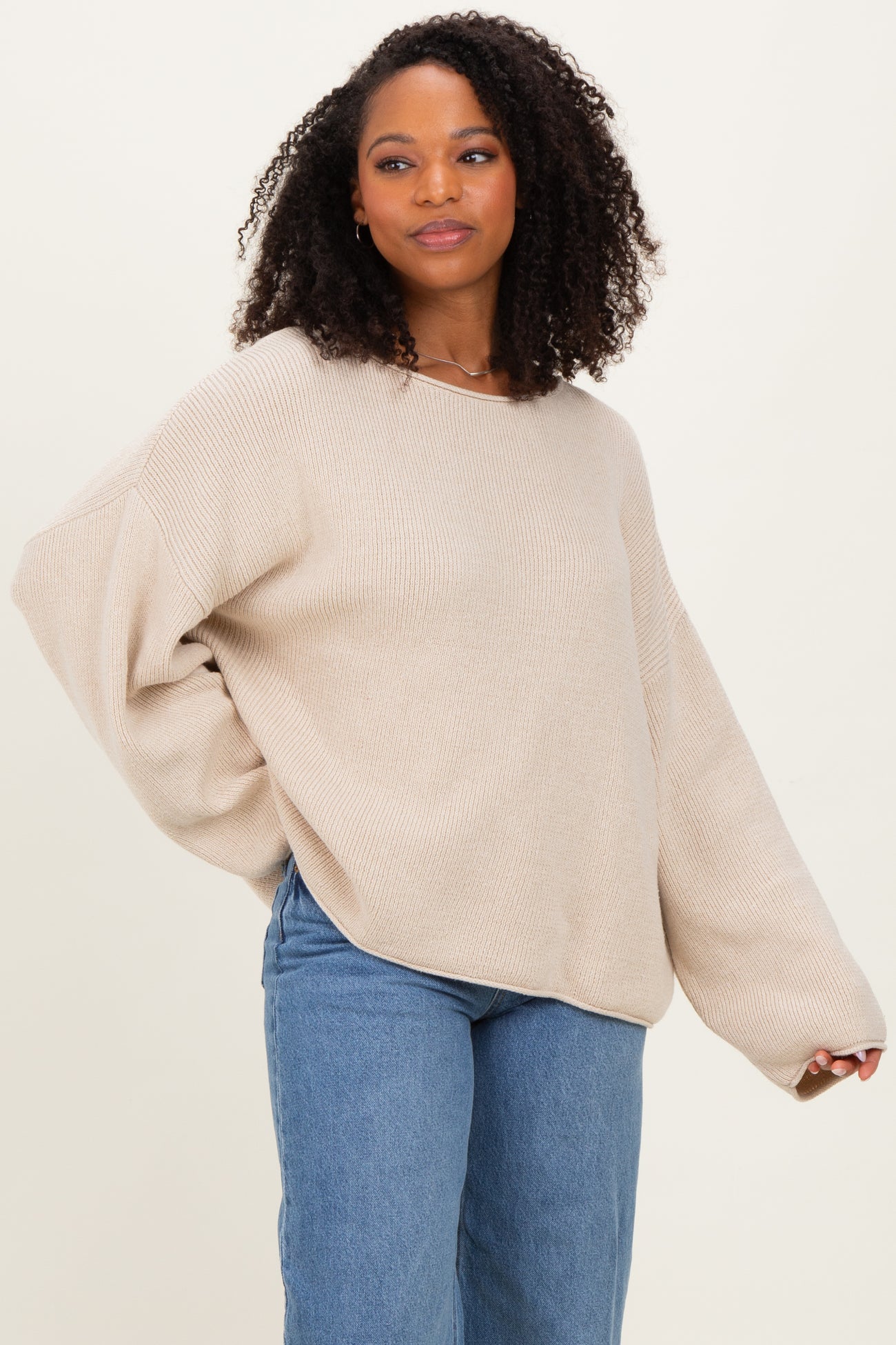 woman wearing a beige oversized sweater with a relaxed fit and long sleeves paired with blue high-waisted jeans