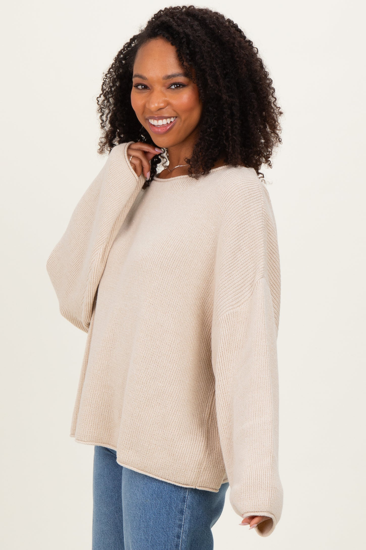 woman wearing a beige oversized knit sweater with long sleeves and relaxed fit paired with blue jeans
