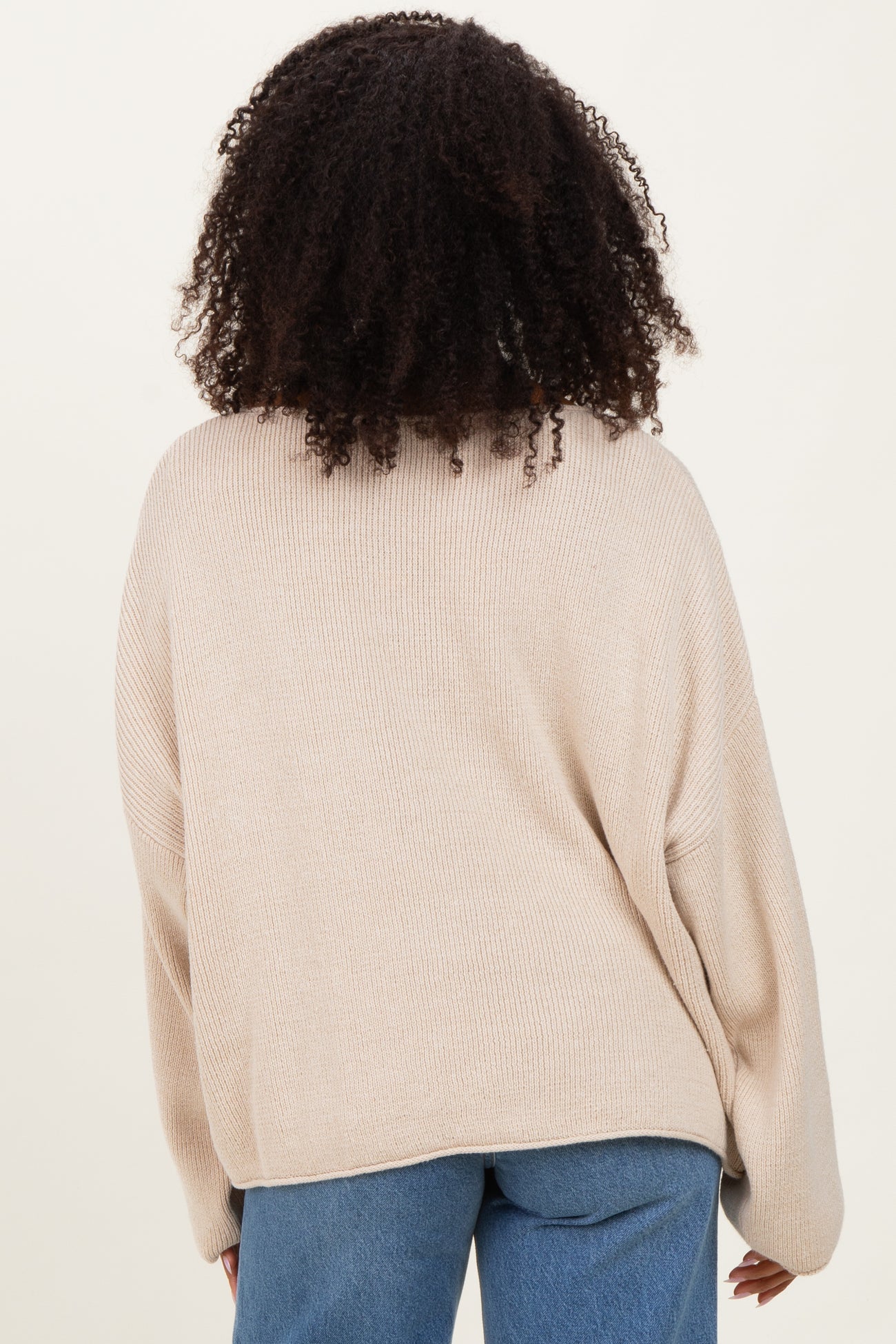 woman wearing a beige oversized knit sweater, seen from the back, paired with light blue jeans