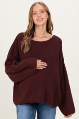 woman wearing a burgundy oversized maternity sweater and gently holding her baby bump