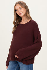 woman wearing a dark burgundy maternity sweater with wide sleeves and a visible baby bump