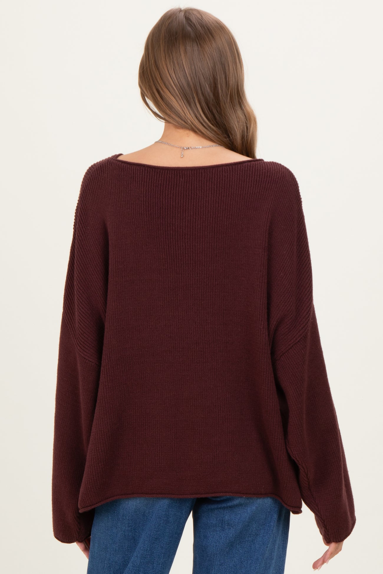 woman wearing a burgundy oversized knitted maternity sweater with a wide neckline and long sleeves, seen from the back
