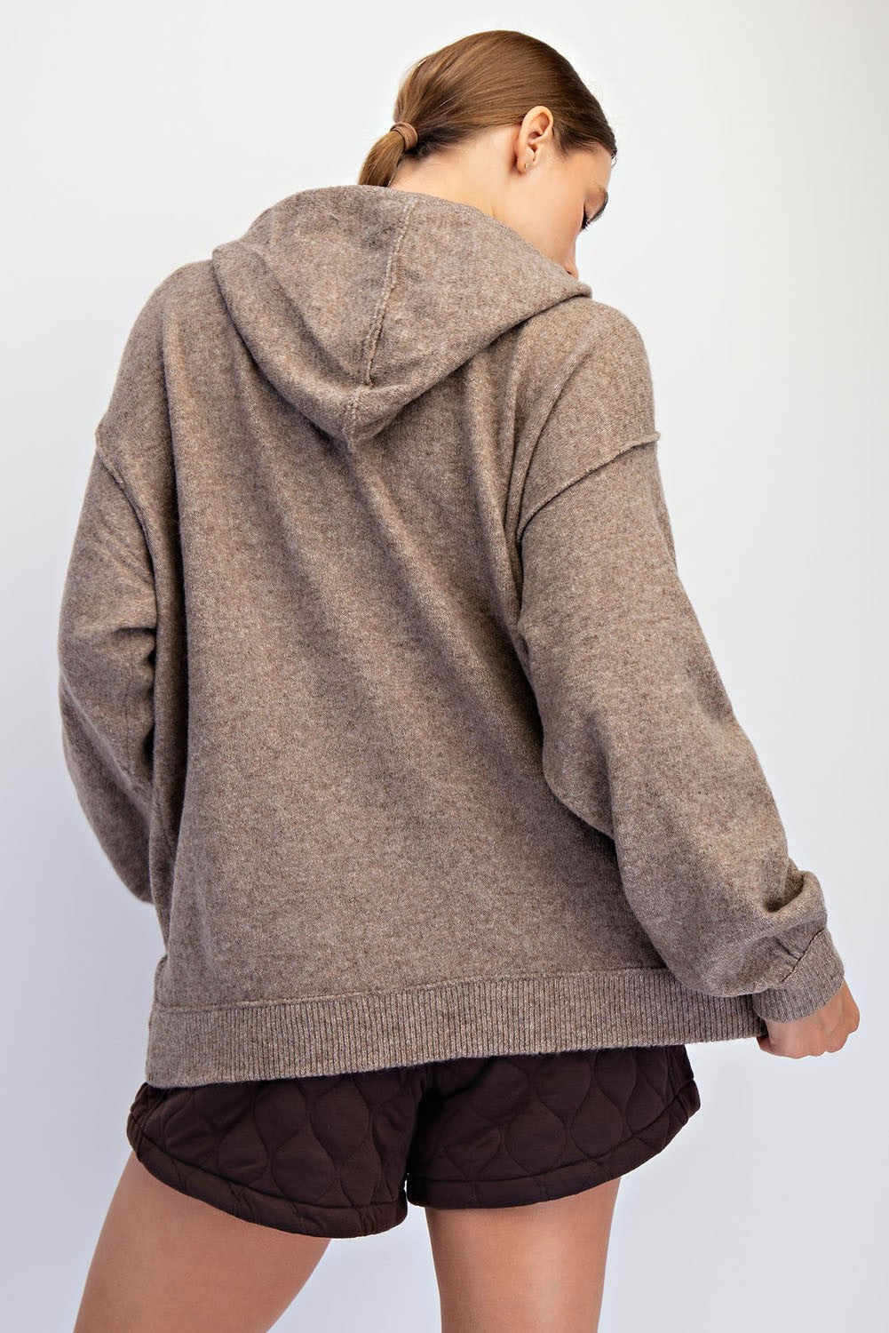 woman wearing a brown oversized hoodie from the back, paired with dark quilted shorts