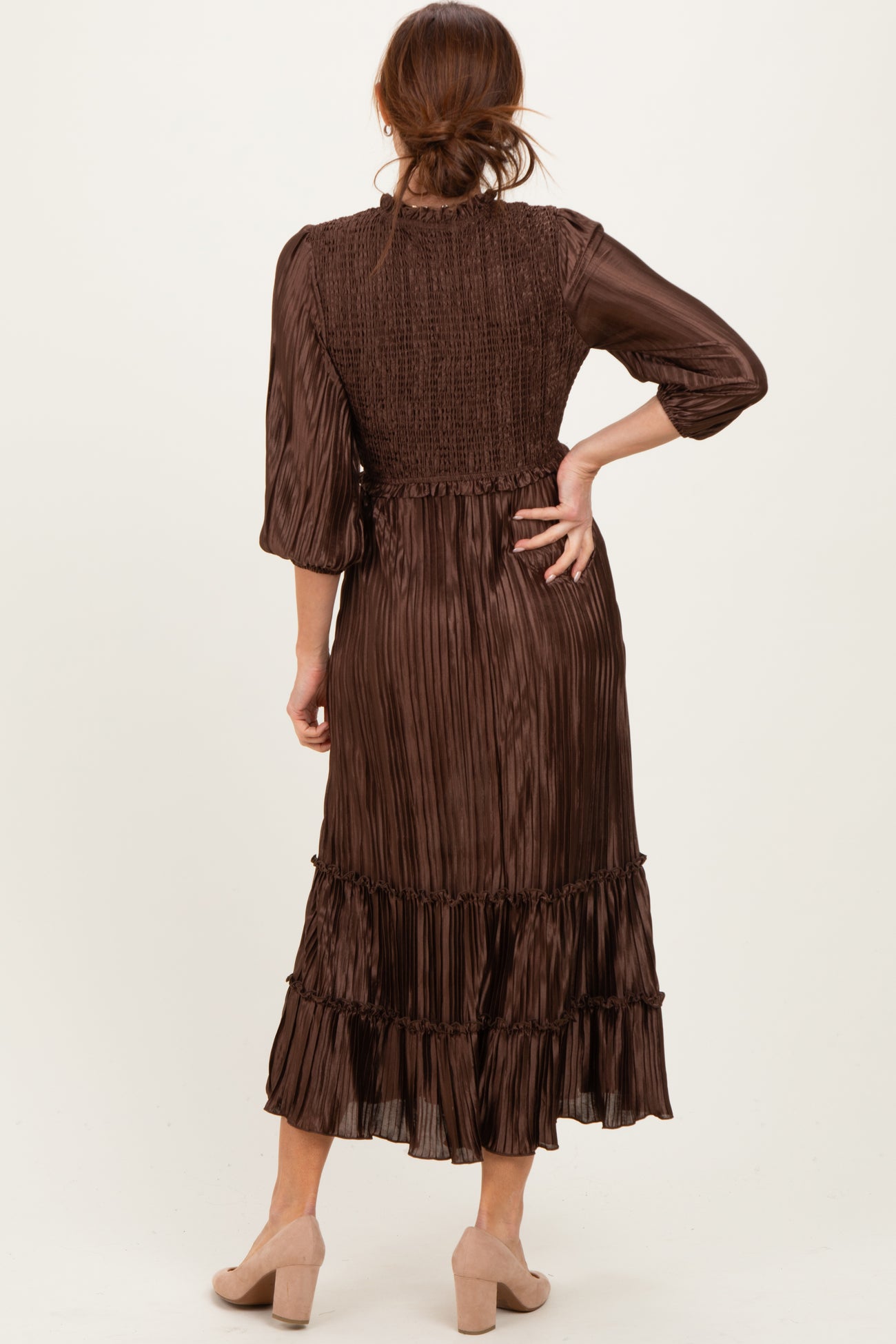 woman wearing a brown pleated midi dress with a smocked bodice and ruffled hem, seen from the back