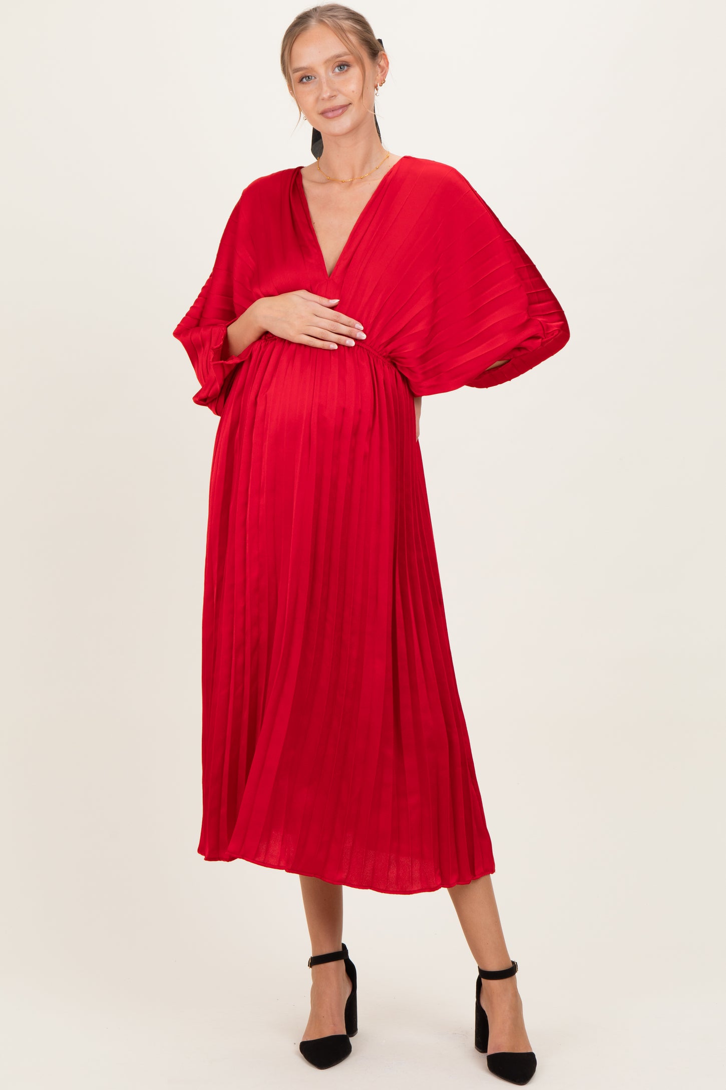 woman wearing a red pleated maternity dress with a deep v-neck and holding her baby bump