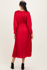 woman wearing a red pleated maternity dress with long sleeves, styled with a tied detail at the back