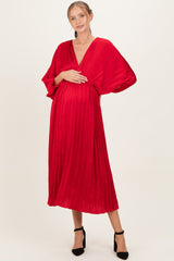 woman wearing a red pleated maternity dress with a deep v-neck and holding her baby bump