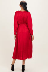 woman wearing a red pleated maternity dress with long sleeves, styled with a tied detail at the back