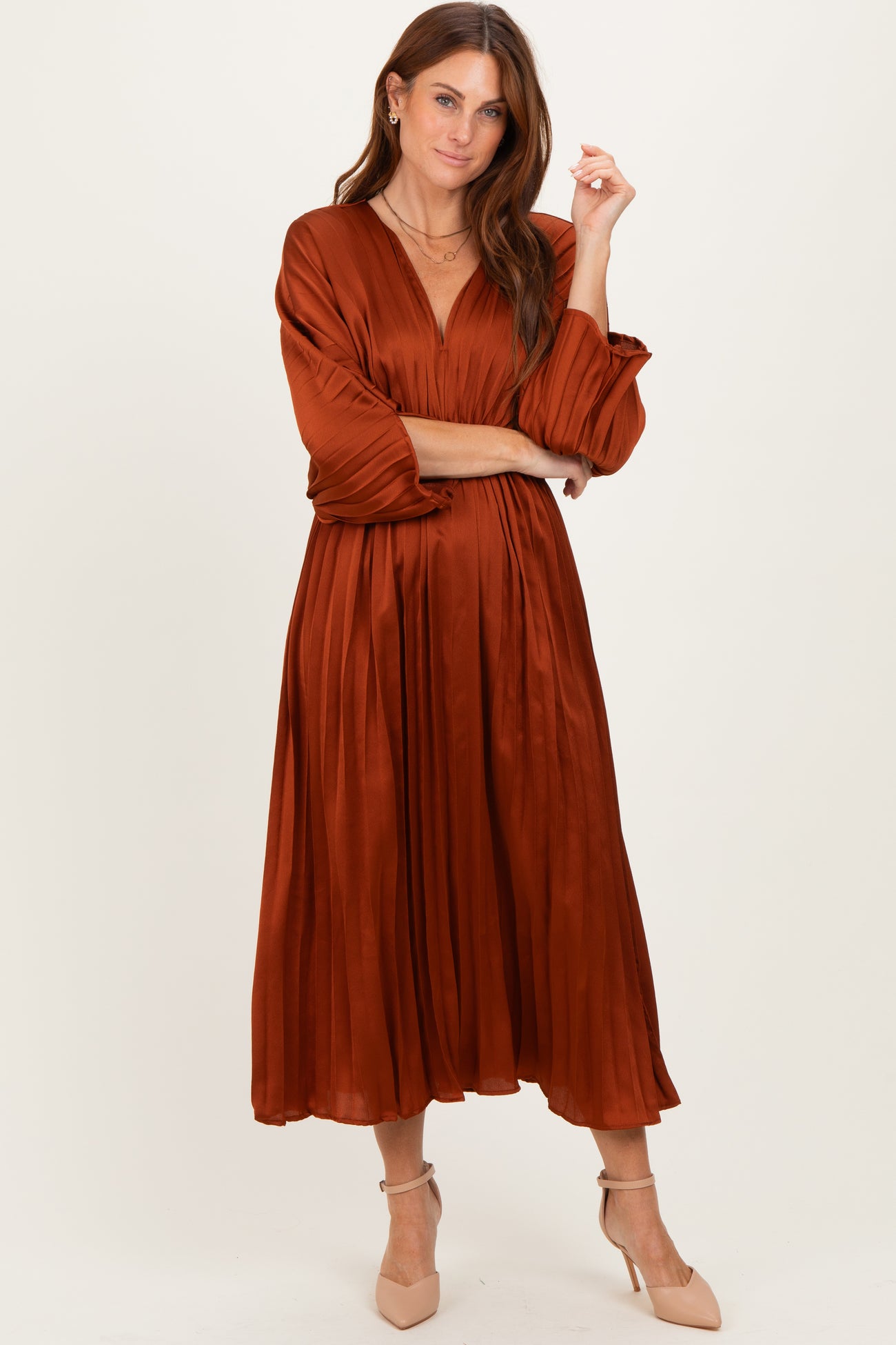woman wearing an rust-colored pleated midi dress with long sleeves and a v-neckline, styled with beige heels