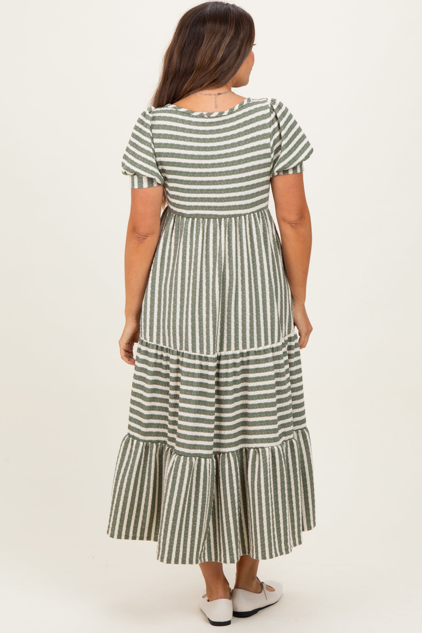 woman wearing a green and white striped maternity maxi dress with short sleeves and a tiered skirt, showing her back