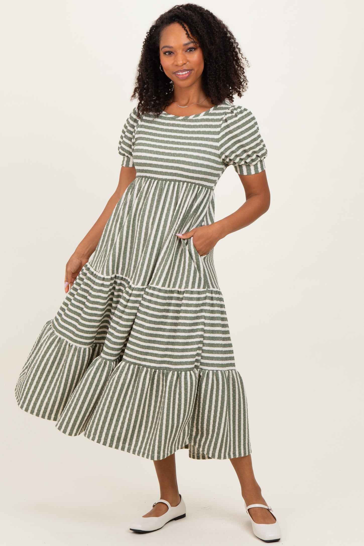 woman wearing a green and white striped maxi dress with short puff sleeves and tiered ruffle hem, posing with hands in pockets
