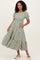 woman wearing a green and white striped maxi dress with short puff sleeves and tiered ruffle hem, posing with hands in pockets