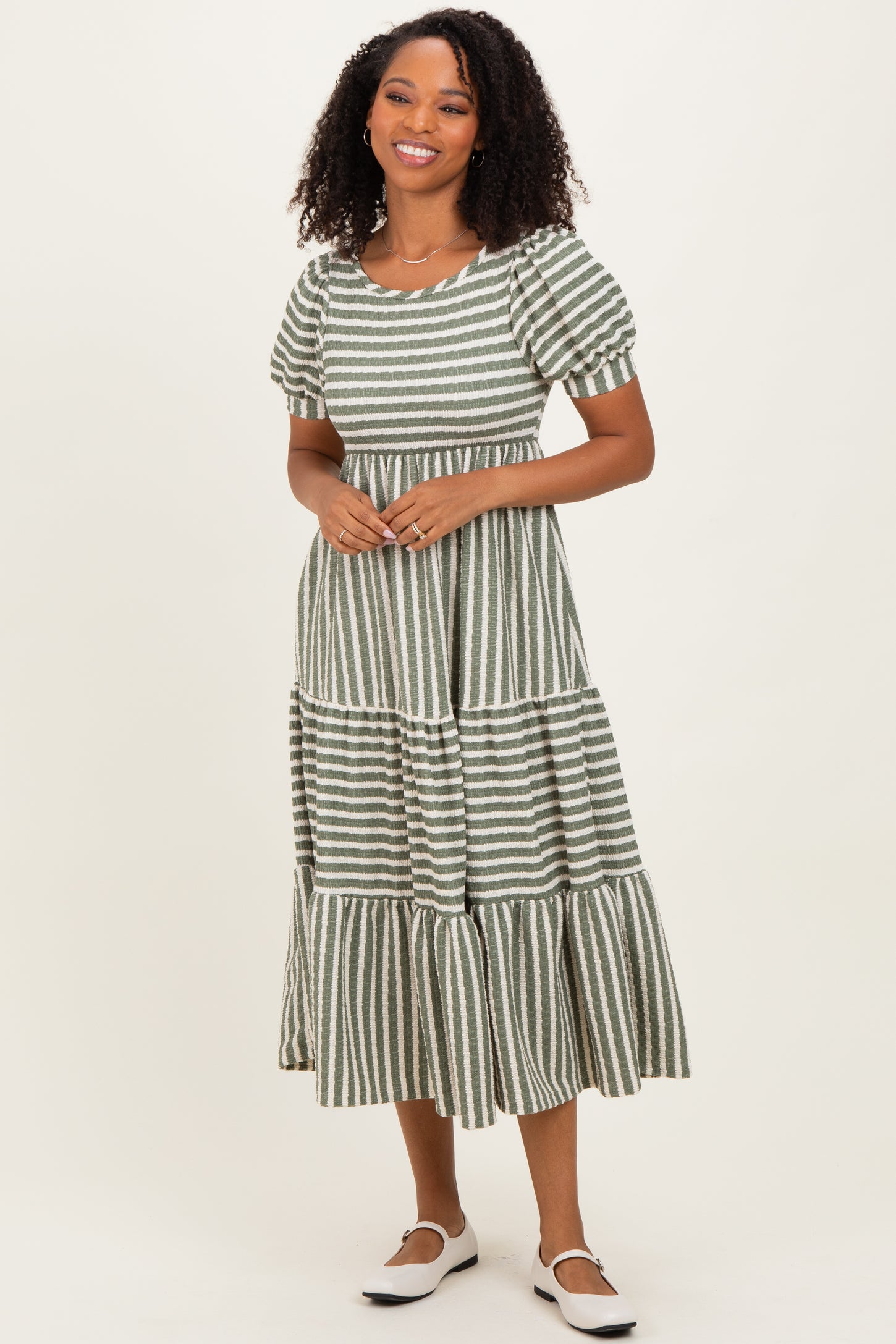 woman wearing a green and white striped midi dress with puff sleeves and a tiered skirt, smiling at the camera