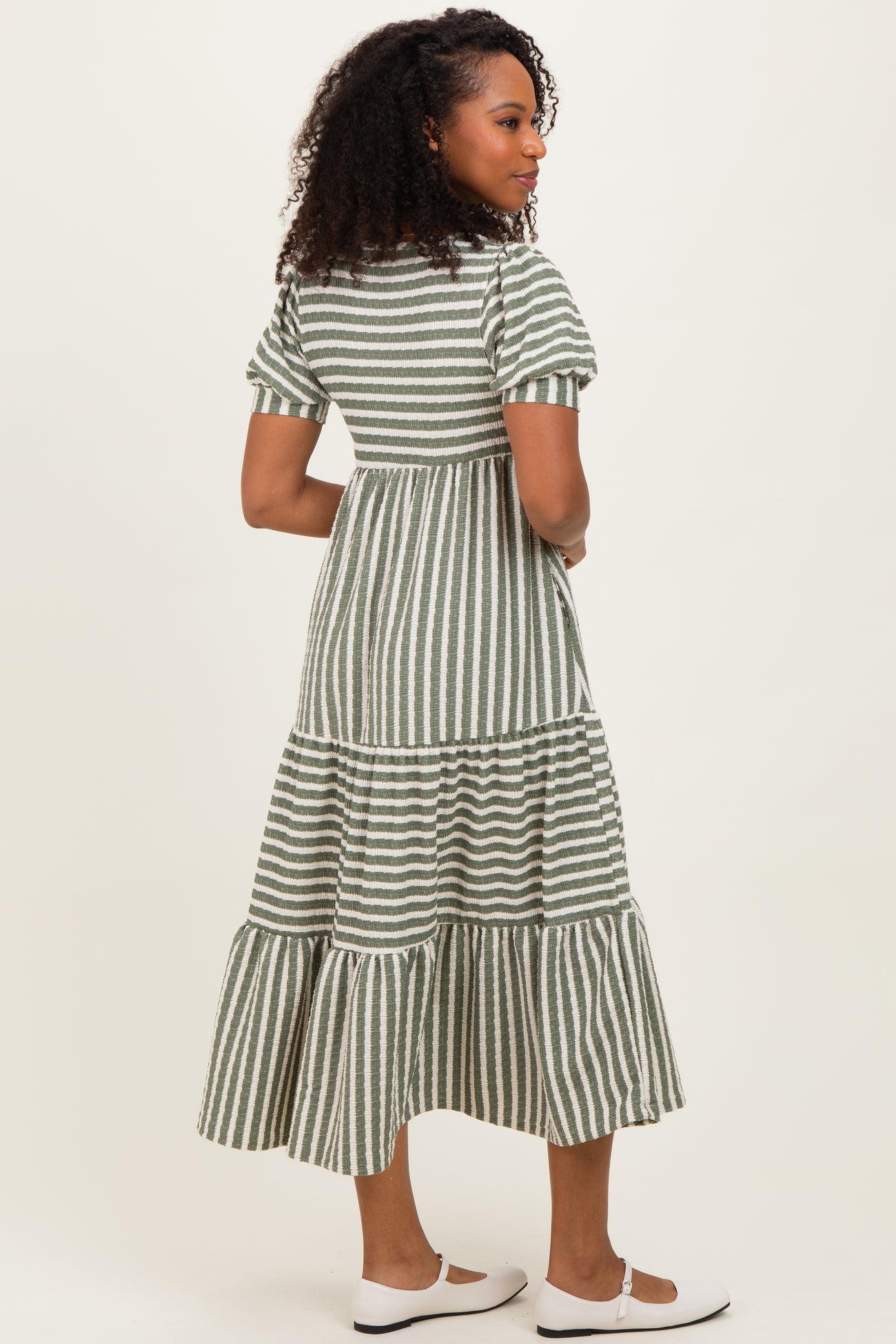 woman wearing a green and white striped midi dress with tiered ruffles and short sleeves, viewed from the back