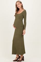 woman wearing a dark olive green long sleeve maternity maxi dress and gently cradling her baby bump