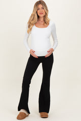 woman wearing a white long sleeve maternity top and black flared pants, holding her baby bump