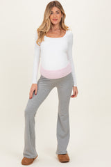 woman wearing a white long sleeve maternity top and gray flared pants, showcasing her baby bump