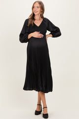 woman wearing a black pleated maternity dress with a v-neck and puff sleeves, holding her baby bump