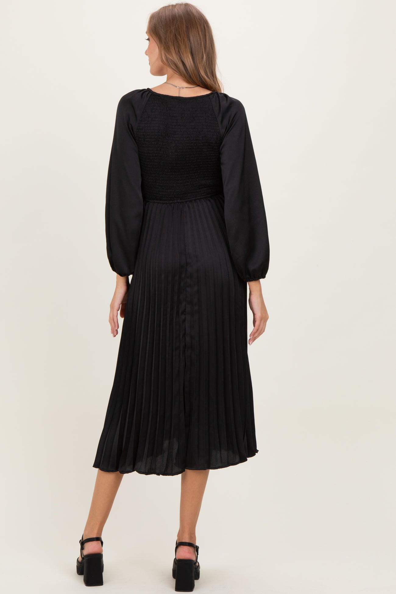 woman wearing a black pleated maternity dress with long sleeves and a smocked bodice, showing the back view