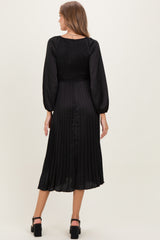 woman wearing a black pleated maternity dress with long sleeves and a smocked bodice, showing the back view
