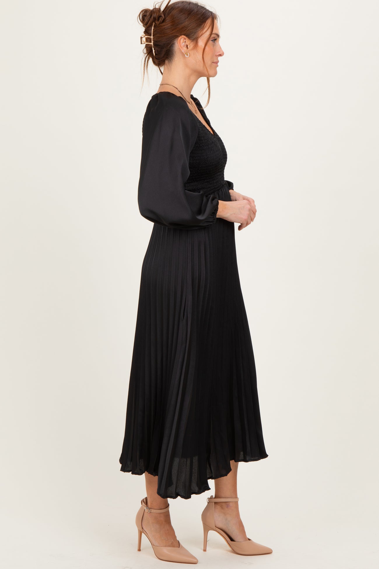 woman wearing a black pleated midi dress with a smocked bodice and long sleeves, styled with nude heels
