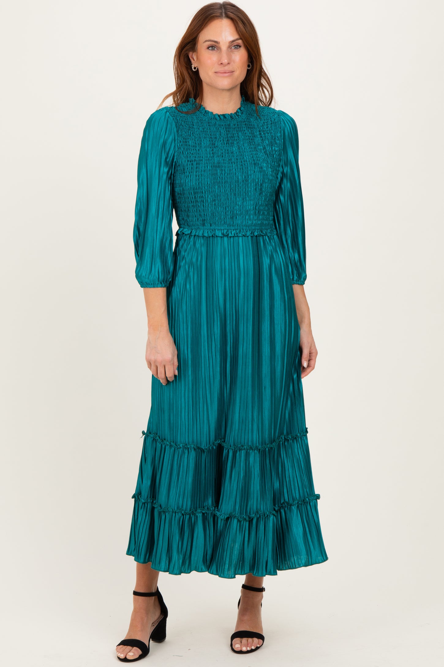 woman wearing a teal pleated maxi dress with smocked bodice and ruffled hem, standing in a relaxed pose