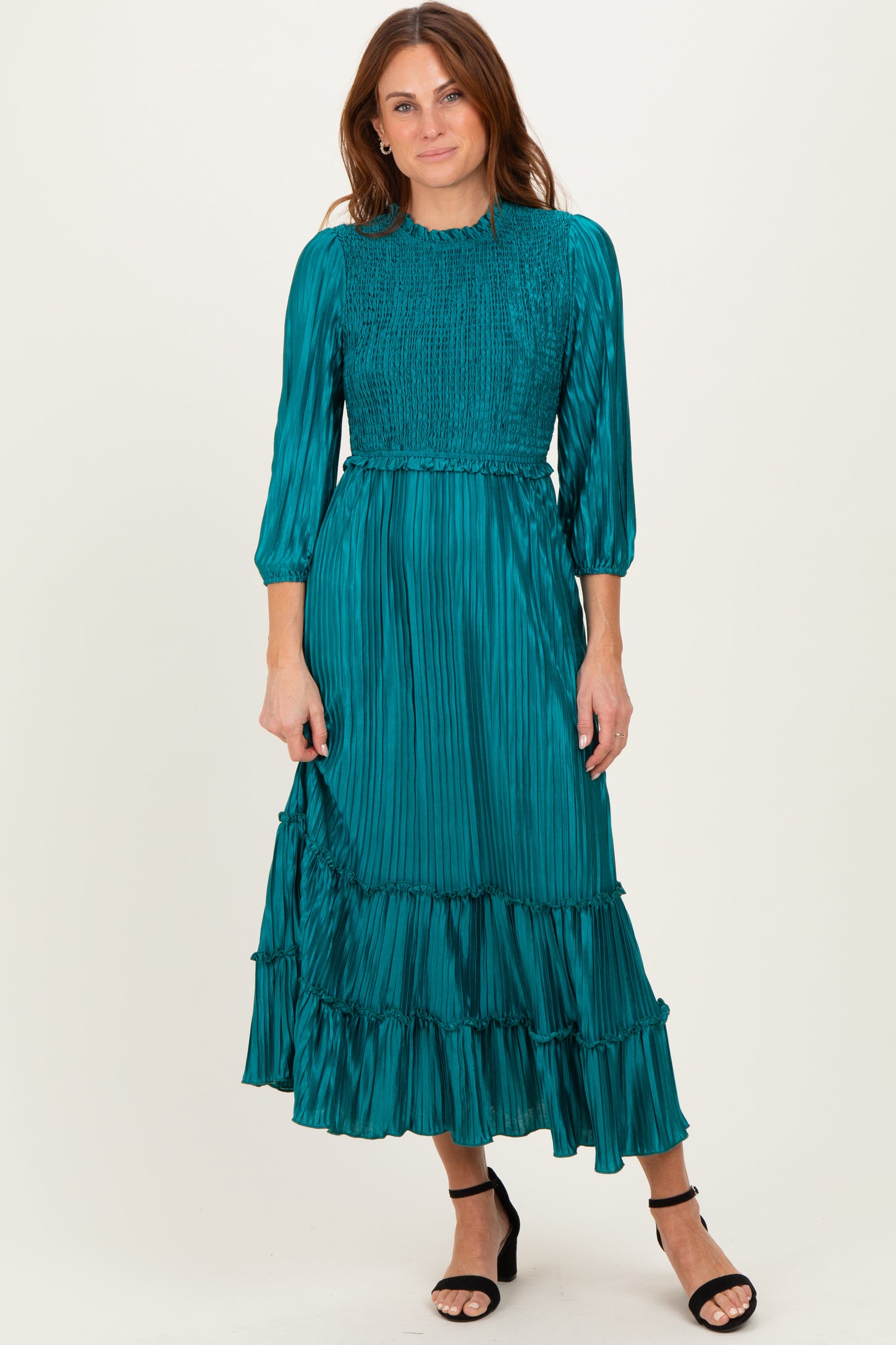 woman wearing a teal pleated midi dress with a smocked bodice and ruffle hem, paired with black strappy heels