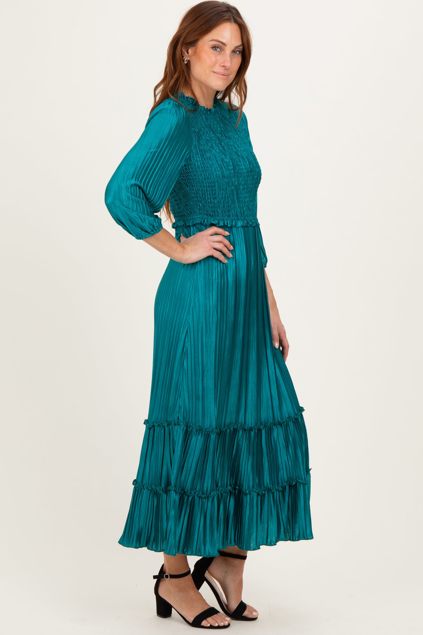 woman wearing a teal pleated maxi dress with a smocked bodice and tiered ruffles, standing in profile