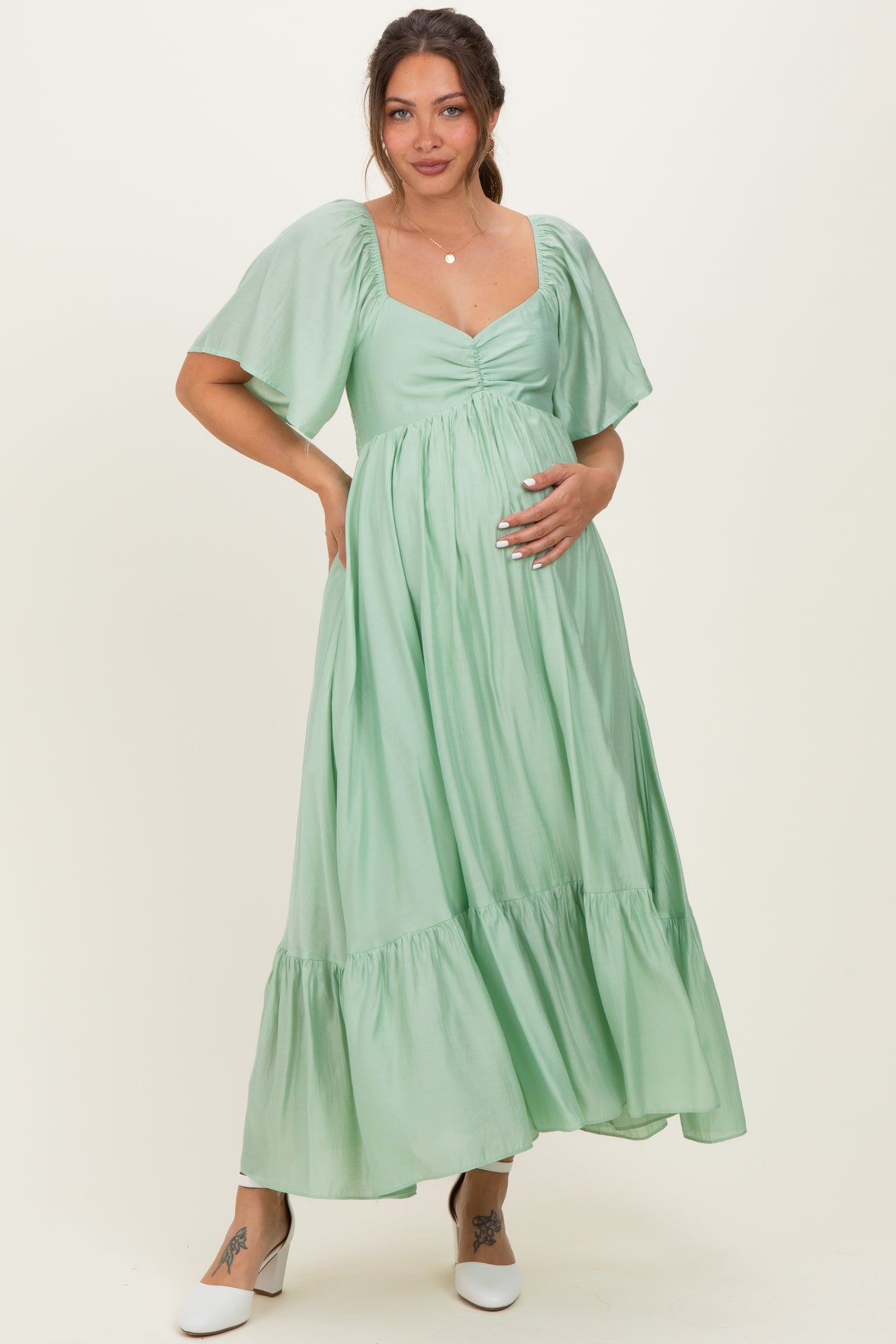 woman wearing a light green maternity maxi dress with puff sleeves and a ruched bodice, holding her baby bump