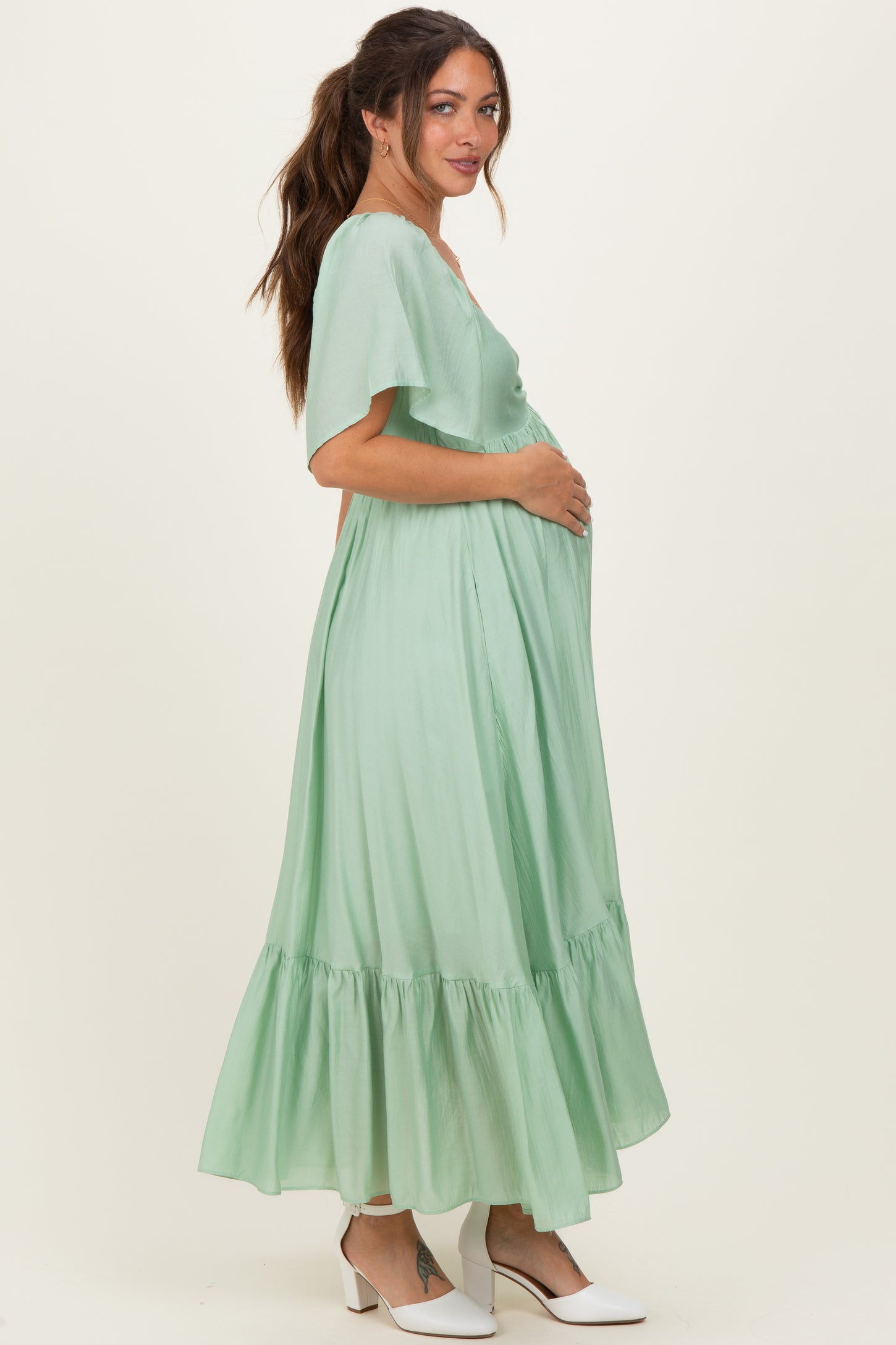 woman wearing a light green maternity dress with short flutter sleeves and a tiered skirt, holding her baby bump