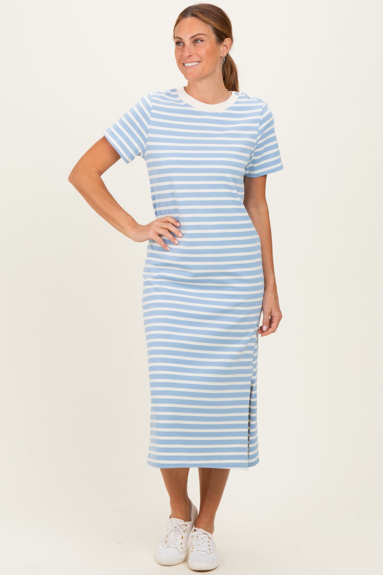 woman wearing a light blue and white striped short sleeve midi dress with a side slit and white sneakers
