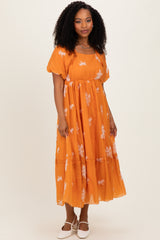 woman wearing an orange floral maxi dress with puff sleeves and a tiered skirt