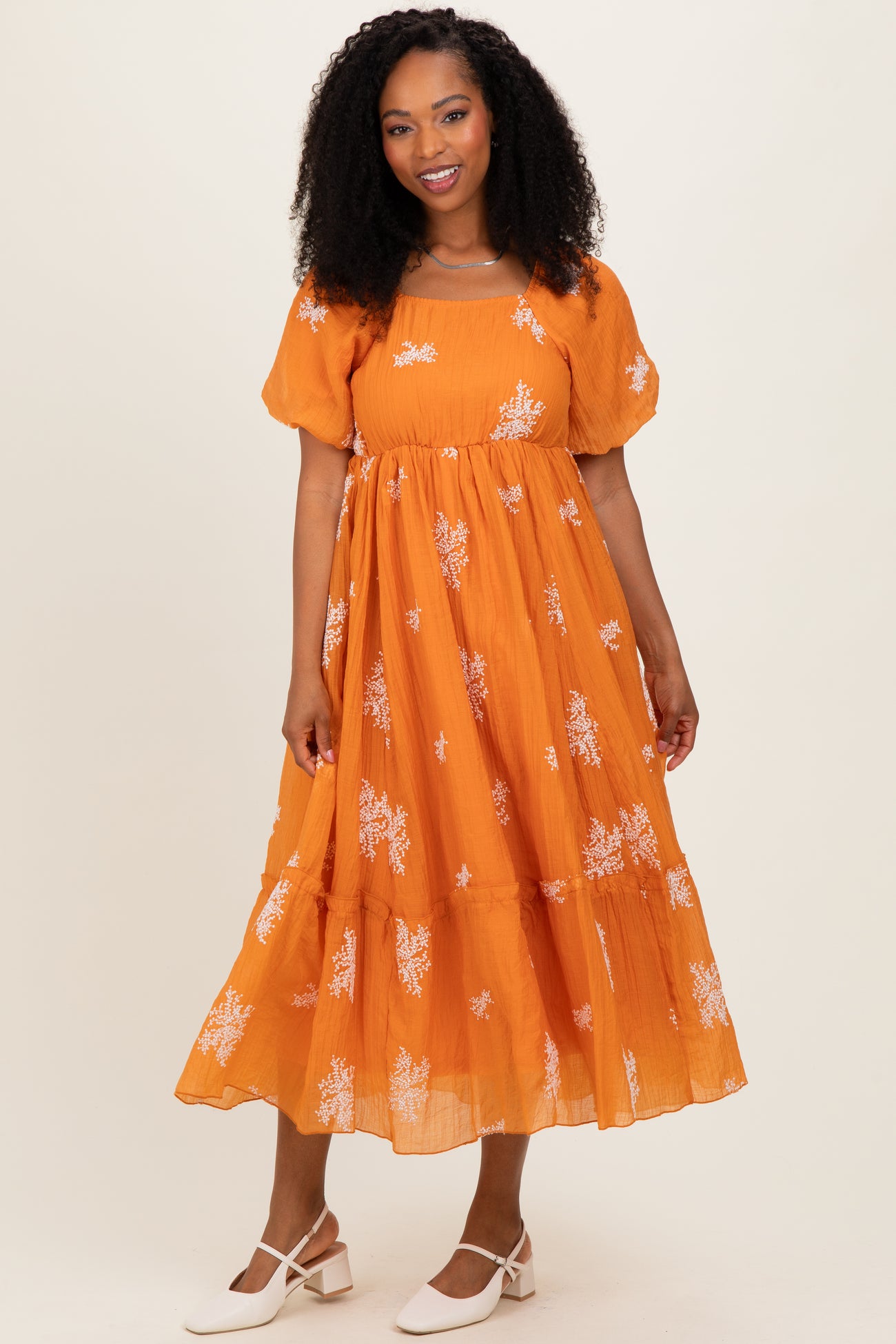 woman wearing an orange floral maxi dress with puff sleeves and a tiered skirt