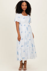 woman wearing a white maxi dress with blue floral prints and short sleeves, standing in a relaxed pose
