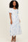 woman wearing a white maxi dress with blue floral prints and short sleeves, standing in a relaxed pose