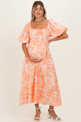 woman wearing a peach floral maternity dress with puff sleeves and holding her baby bump