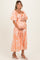 woman wearing an apricot floral maternity maxi dress, holding her baby bump with a smile