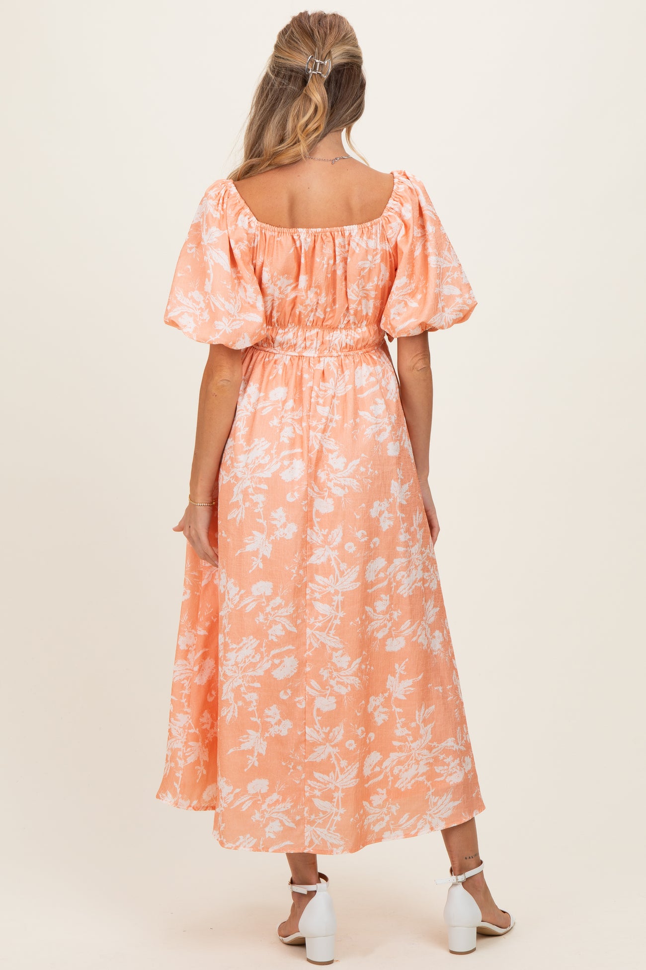 woman wearing a floral patterned orange maternity dress with puff sleeves and a smocked waist, showing her back