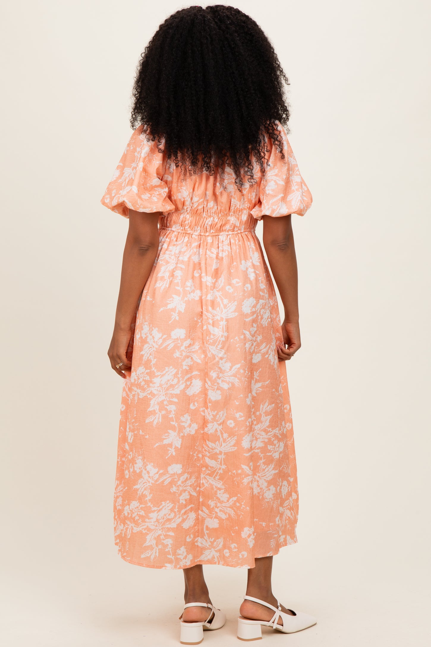 woman wearing an orange floral maxi dress with puff sleeves and a smocked waist, viewed from the back