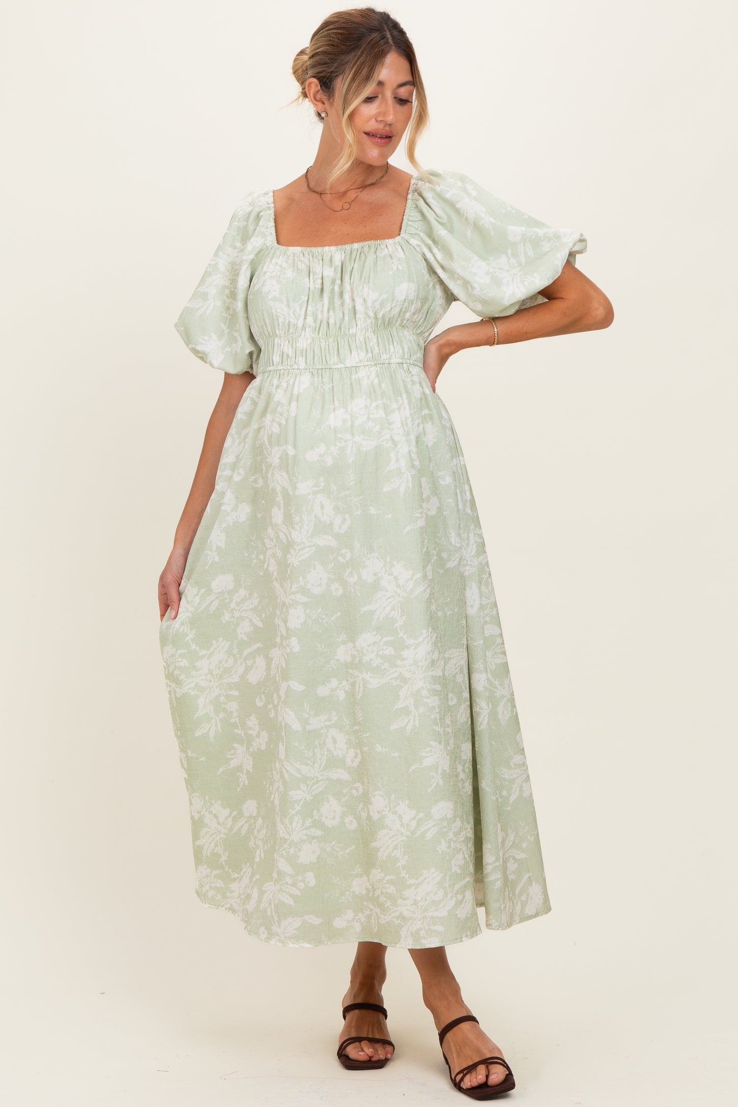 woman wearing a light green floral maternity dress with puff sleeves and a square neckline, showcasing a baby bump