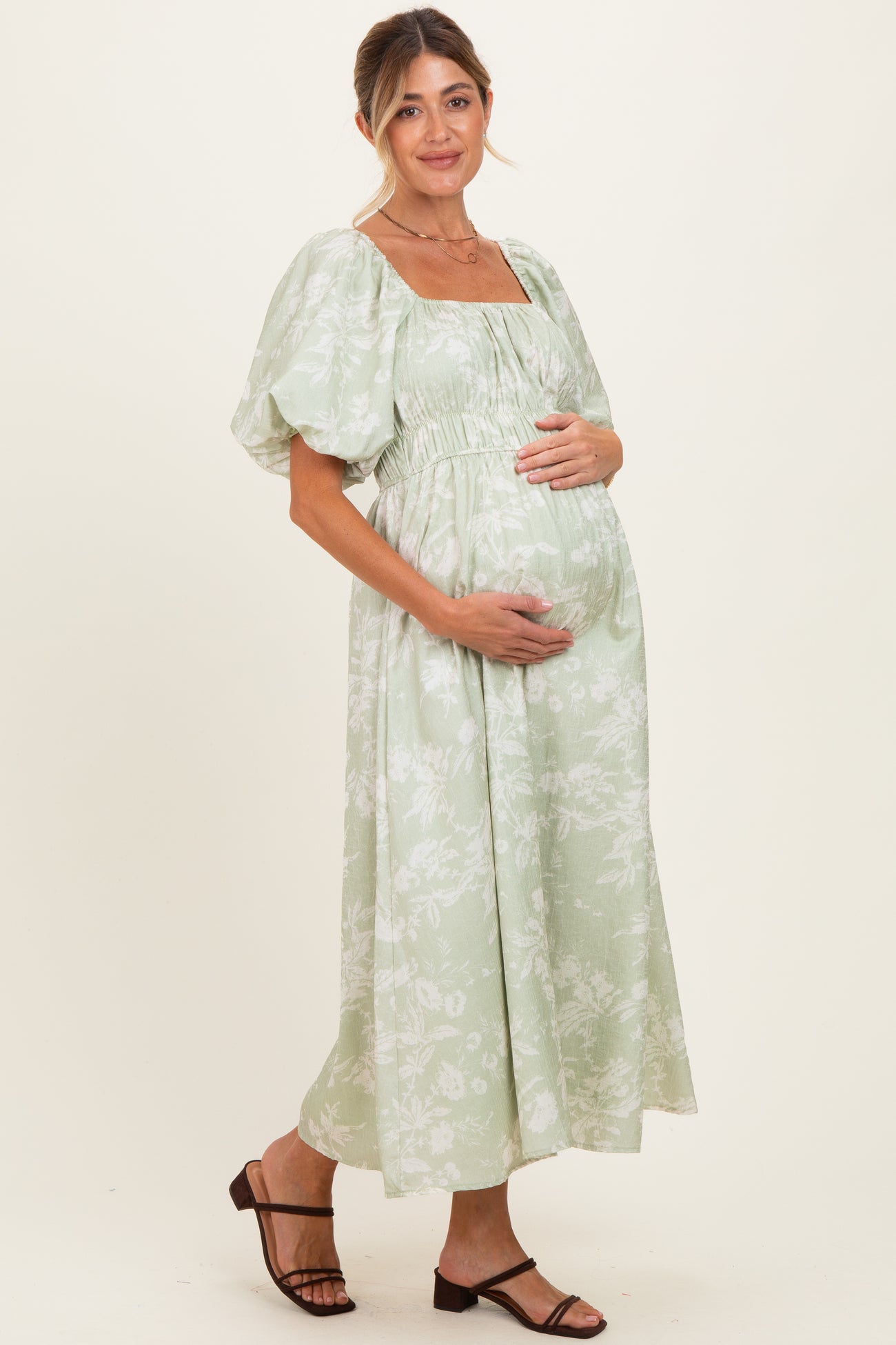 woman wearing a light green floral print maternity dress with puff sleeves and a visible baby bump