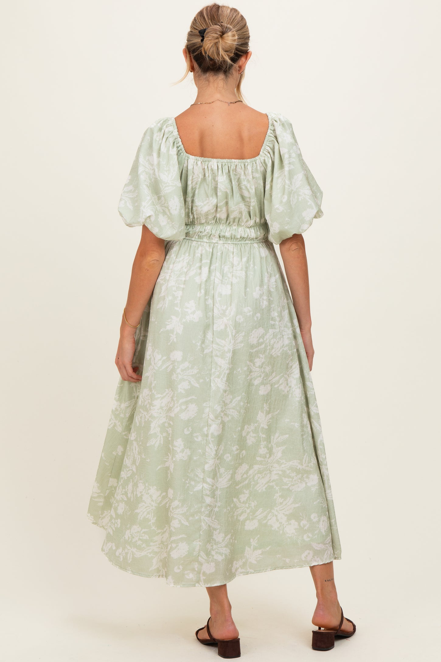 woman wearing a light green floral maternity dress with puff sleeves and a cinched waist, showing an elegant back view