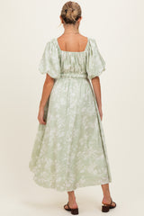woman wearing a light green floral maternity dress with puff sleeves and a cinched waist, showing an elegant back view